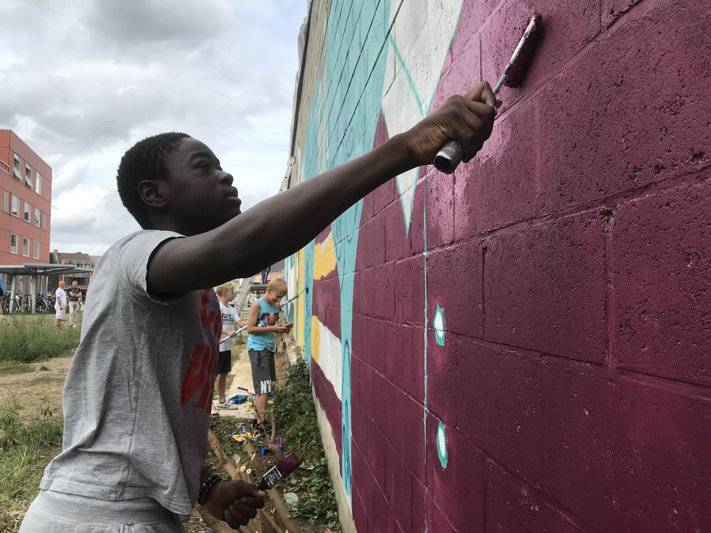 A boy stretching up to paint a mural with a roller